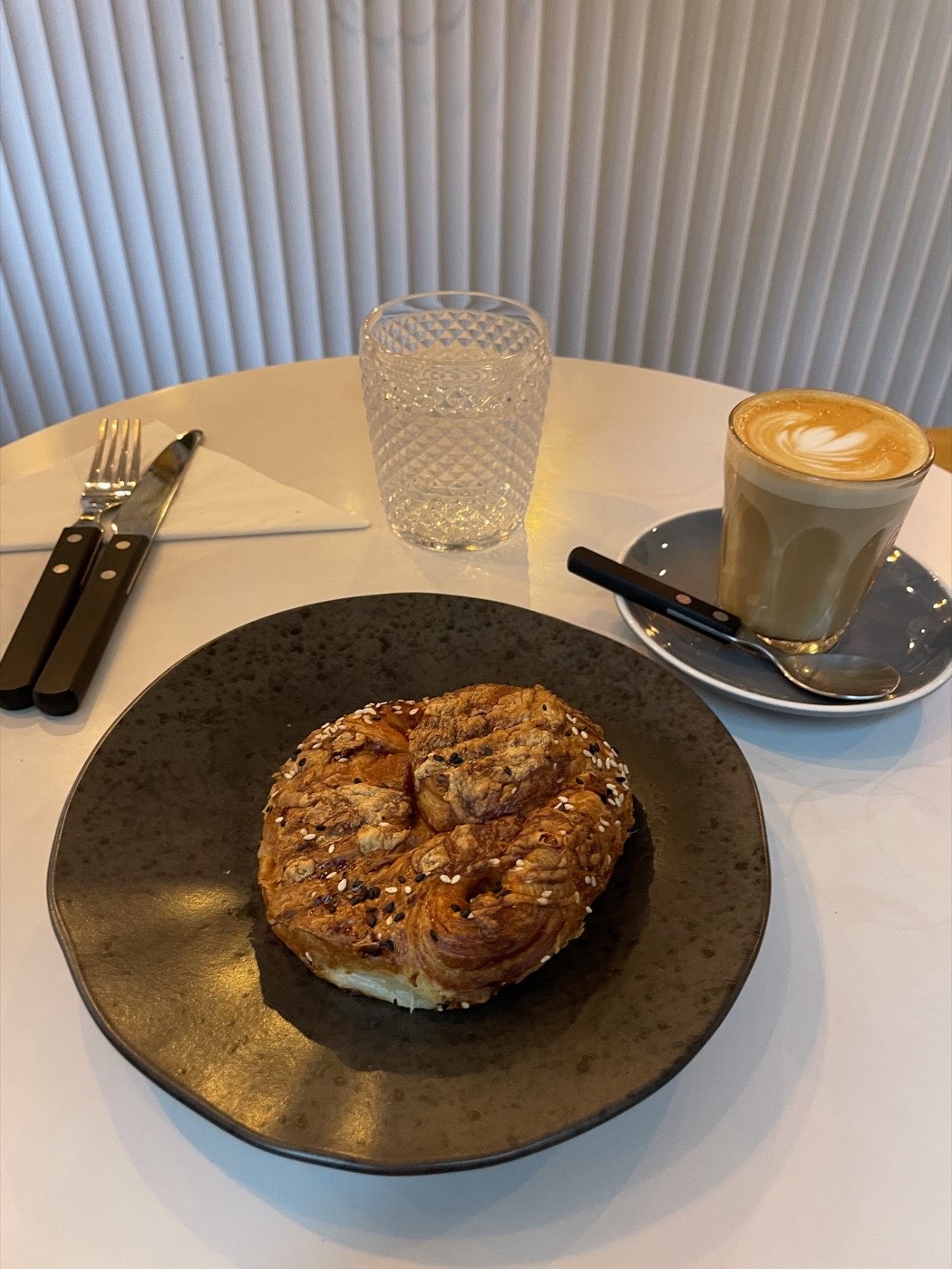 A seeded pastry served with a flat white at a table inside Rise & Bloom